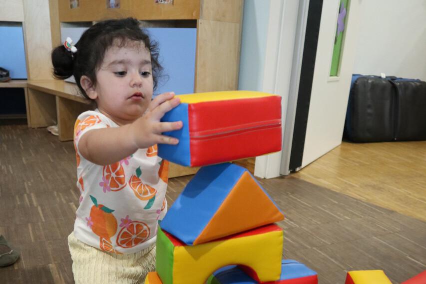 Kleines Kind stapelt bunte Bauklötze auf einem Holzboden in einem Spielzimmer.