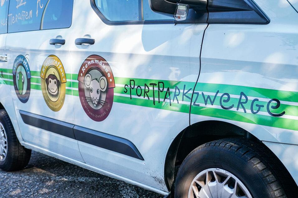 Seitenansicht eines Fahrzeugs mit farbigen Emblemen und dem Schriftzug "Sportparkzwerge" auf einer weißen Karosserie.