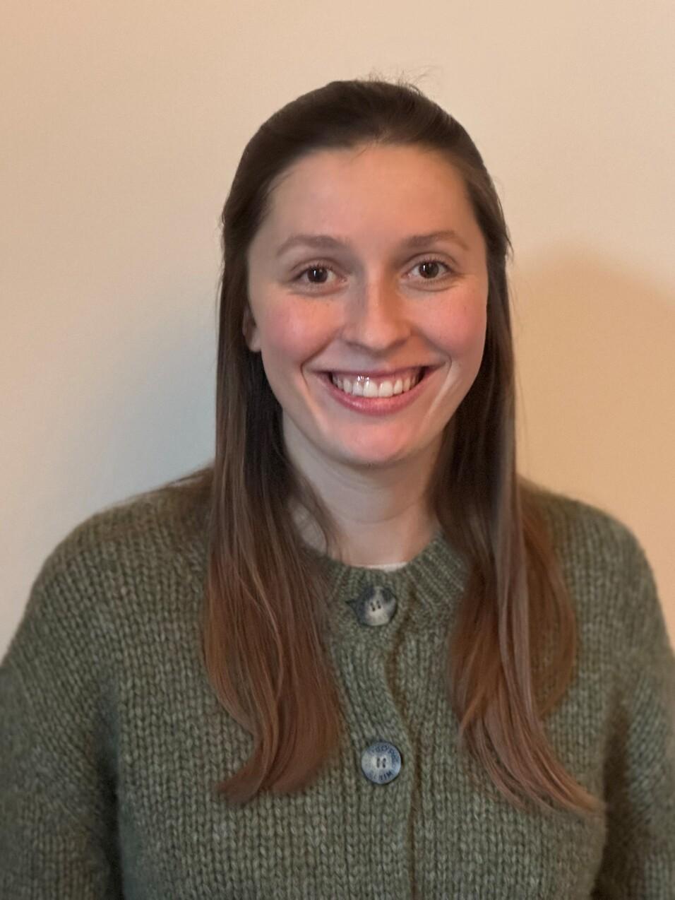 Porträt einer lächelnden Person mit langen, glatten braunen Haaren, die offen über die Schultern fallen